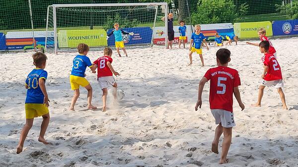 Kinder spielen Fußball im Sand.