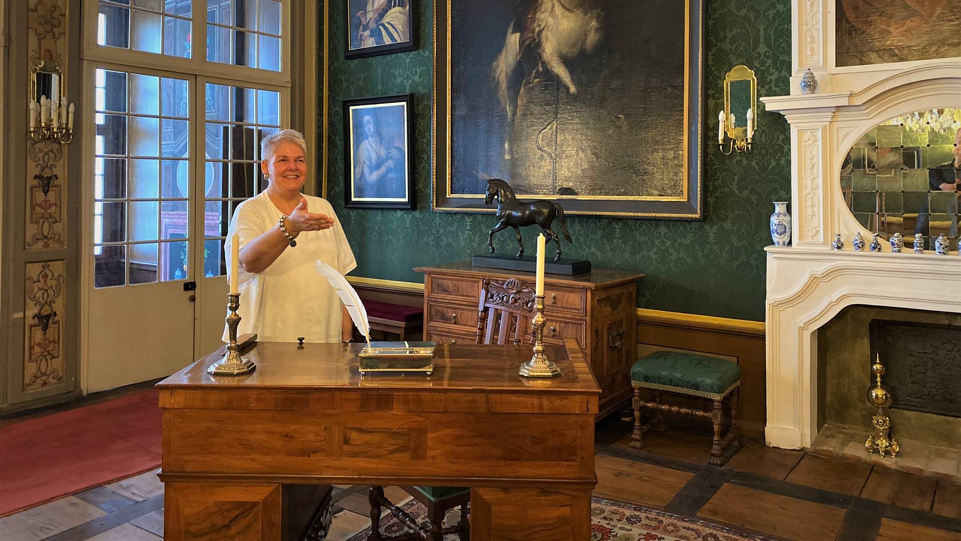 Eine Frau steht in einem historisch eingerichtete Zimmer mit SChreibtisch und Gemälden