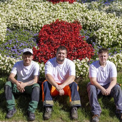 Drei junge Menschen sitzen vor einem Blumenbeet, das das Wolfenbütteler Stadtwappen darstellt