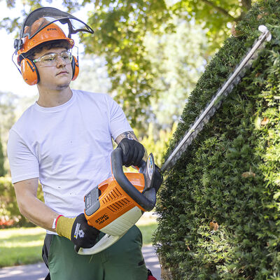 Ein junger Gärtner bearbeitet einen Busch mit einer elektrischen Heckenschere