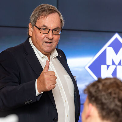 Ein Mann spricht vor Publikum, im Hintergrund eine Leinwand mit dem Logo der Firma MKN