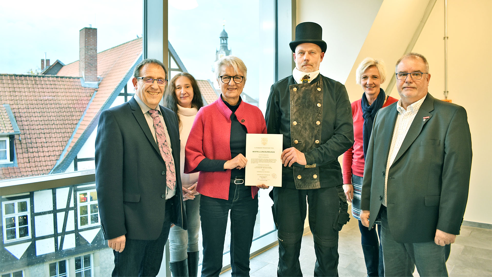 Gruppenfoto mit drei Frauen und drei Männern, davon einer in Schornsteinfeger-Kleidung. Eine der Frauen überreicht dem Schornsteinfeger eine Urkunde.