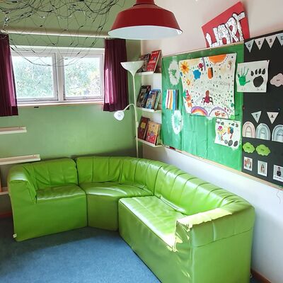 Ein Kitaraum mit einer grünen Ledercouch, an der Wnd hängen Kinderzeichnungen und in der Ecke steht ein Regal mit Ordnern