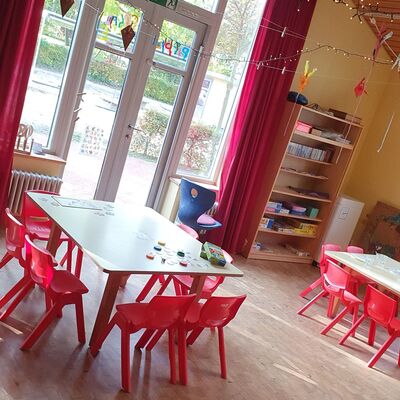 Ein Zimmer in der Kita mit Kindertischen und roten Kinderstühlen