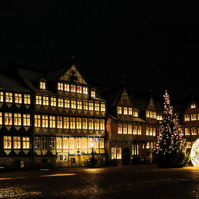 Das Wolfenbütteler Rathaus ist mit vielen leuchtenden Lichterbögen in den Fenstern geschmückt, auf dem Stadtmarkt davor steht eine große beleuchtete Tanne und eine leuchtende überdimensionale Weihnachtskugel.