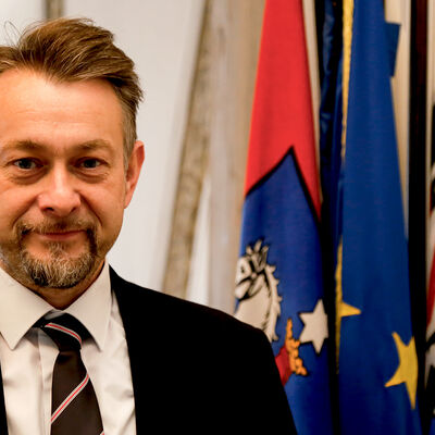 Porträt des Bürgermeisters Ivica Lukanic, im Hintergrund hängt die Stadtfahne an einem Fahnenständer.