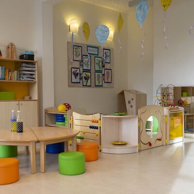 Kita-Raum mit Spielecke, Tisch mit Sitzhockern, Schrank mit Büchern