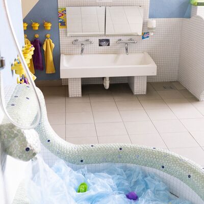 Kita-Badezimmer mit Spielecke und Waschbecken, Handtüchern, Zahnputzbechern