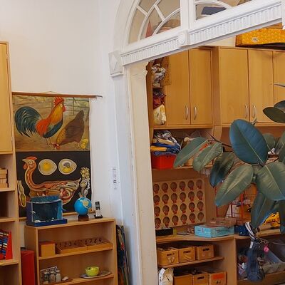 Ein Kita-Raum mit Schänken und Regalen, gefüllt mit Spielsachen, und einem Hühnerbild an der Wand.