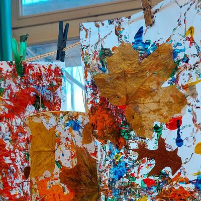 An einer Wäscheleine hängen Papierbögen, auf denen mit Farbe und getrockneten Blättern Kunstwerke geschaffen worden sind.