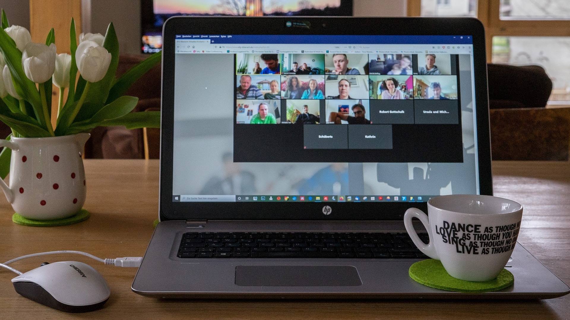 Auf dem Monitor eines Laptops sind mehrere Teilnehmerbilder einer Online-Konferenz zu sehen.