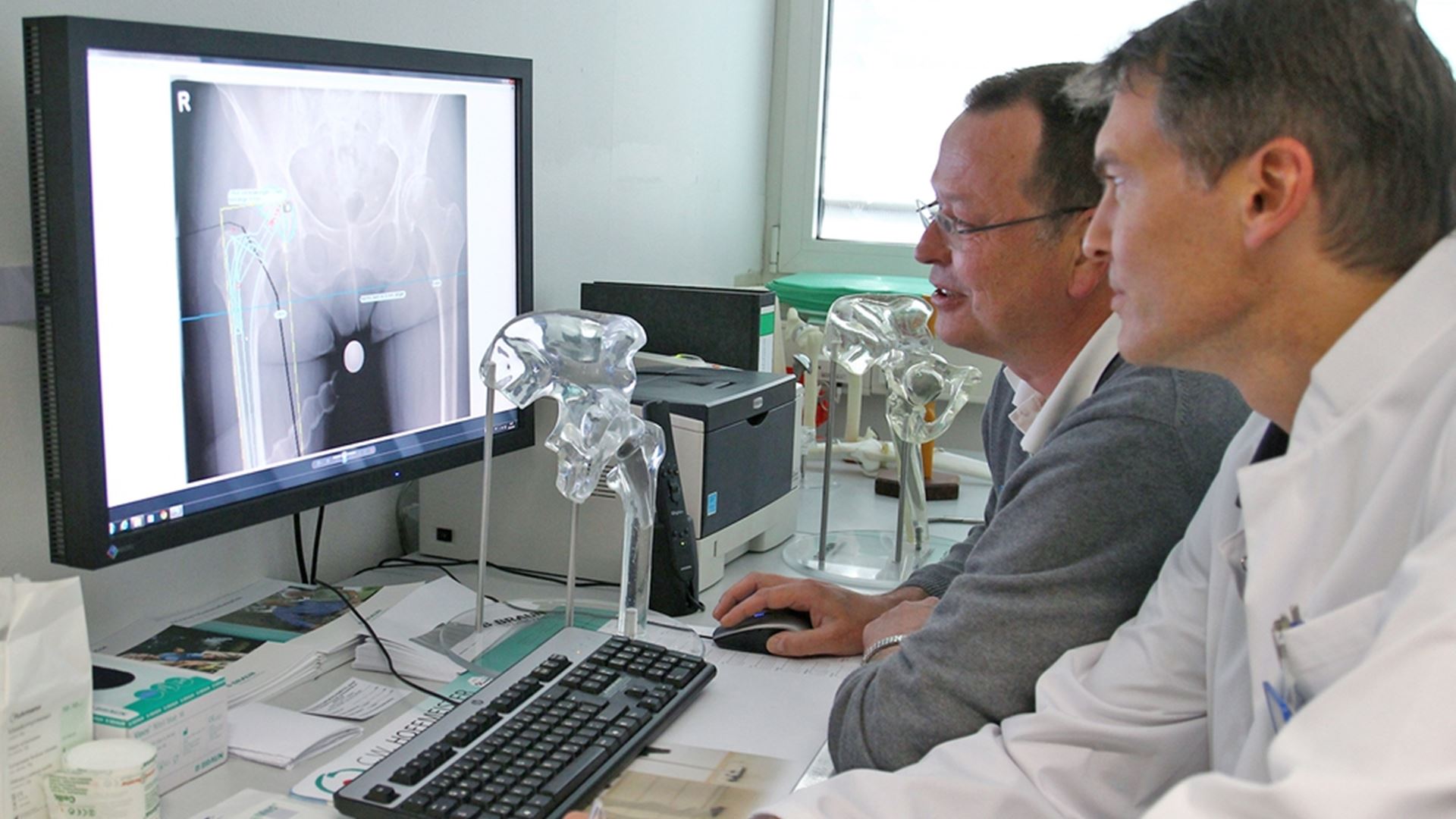 Zwei Ärzte sitzen vor einem Monitor und schauen sich ein Röntgenbild an.