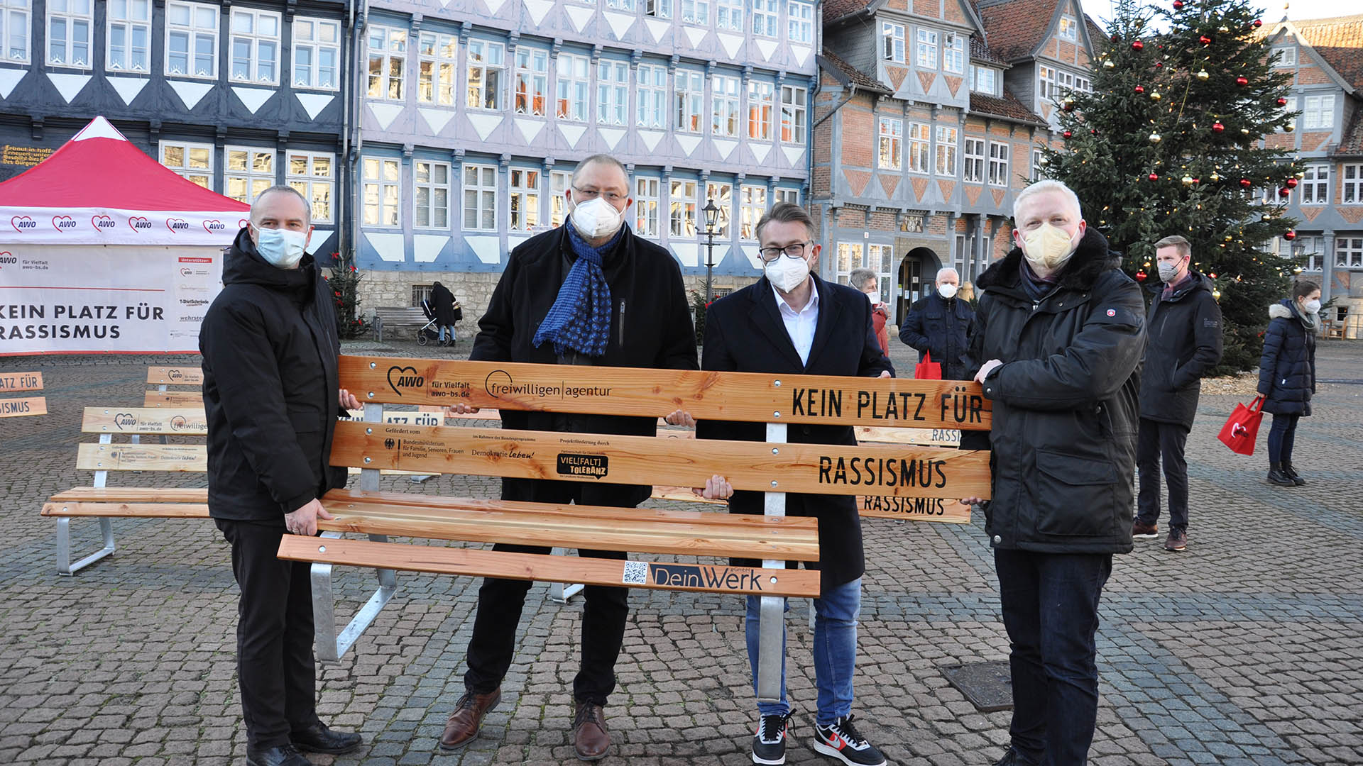Vier Männer stehen auf dem Stadtmarkt vor dem Rathaus und tragen eine Holzbank mit der Aufschrift Kein Platz für Rassismus.