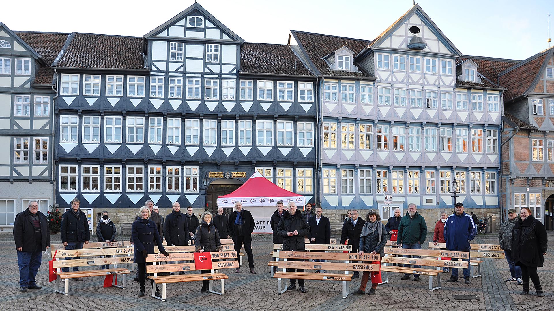 Viele Menschen stehen verteilt auf dem Stadtmarkt vor dem Rathaus, zwischen ihnen stehen Holzbänke mit der Aufschrift Kein Platz für Rassismus.