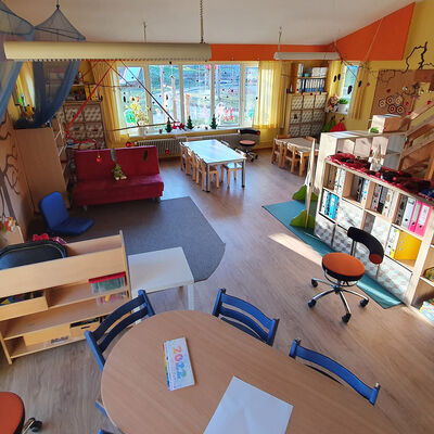 Blick in einen großen Raum mit Spielzeug, Tischen und Stühlen und Regalen.
